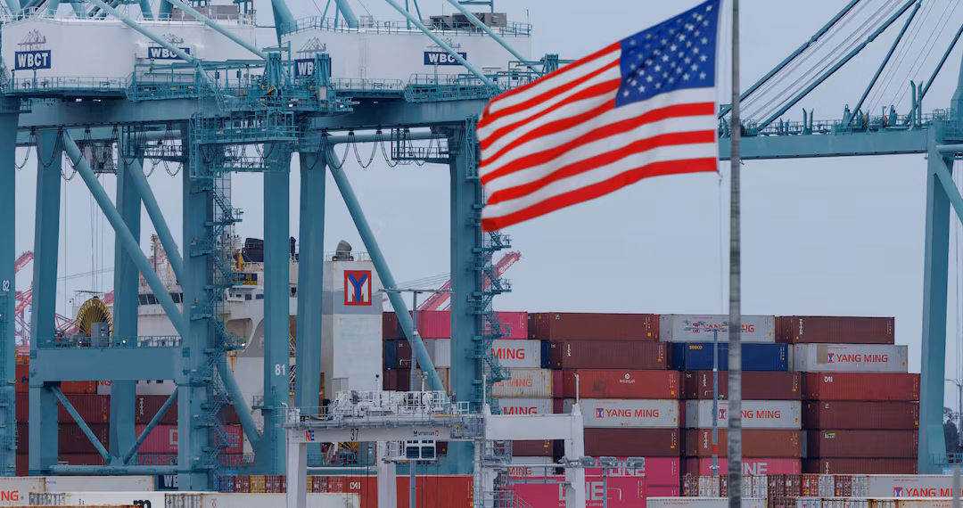 ১ মে, ২০২৫ তারিখে ক্যালিফোর্নিয়ার সান পেড্রোর লস অ্যাঞ্জেলেস বন্দরে জাহাজের মালামাল খালাসের সময় শিপিং কন্টেইনারের কাছে একটি মার্কিন পতাকা উড়ছে। রয়টার্স