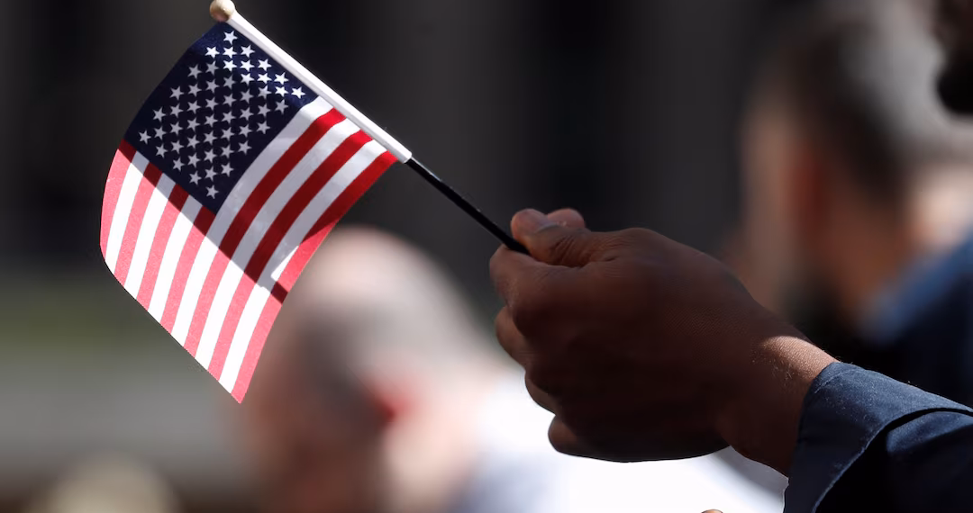 ১৭ সেপ্টেম্বর, ২০১৯, নিউ ইয়র্ক সিটির রকফেলার প্লাজায় মার্কিন নাগরিকত্ব ও অভিবাসন পরিষেবা (USCIS) নাগরিকত্ব প্রদান অনুষ্ঠানে একজন নাগরিকত্ব প্রার্থী পতাকা ধরে আছেন। রয়টার্স